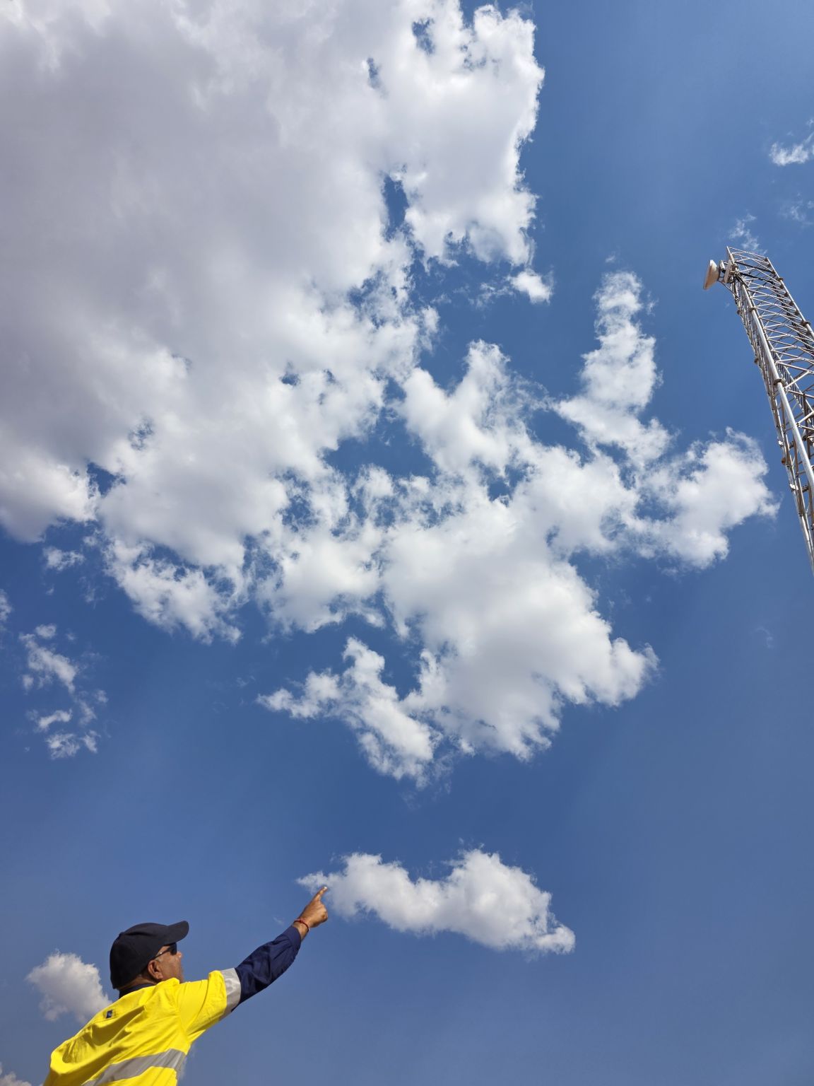 APD Global field technician in hi-vis pointing up at a lattice communications tower on a remote mine site